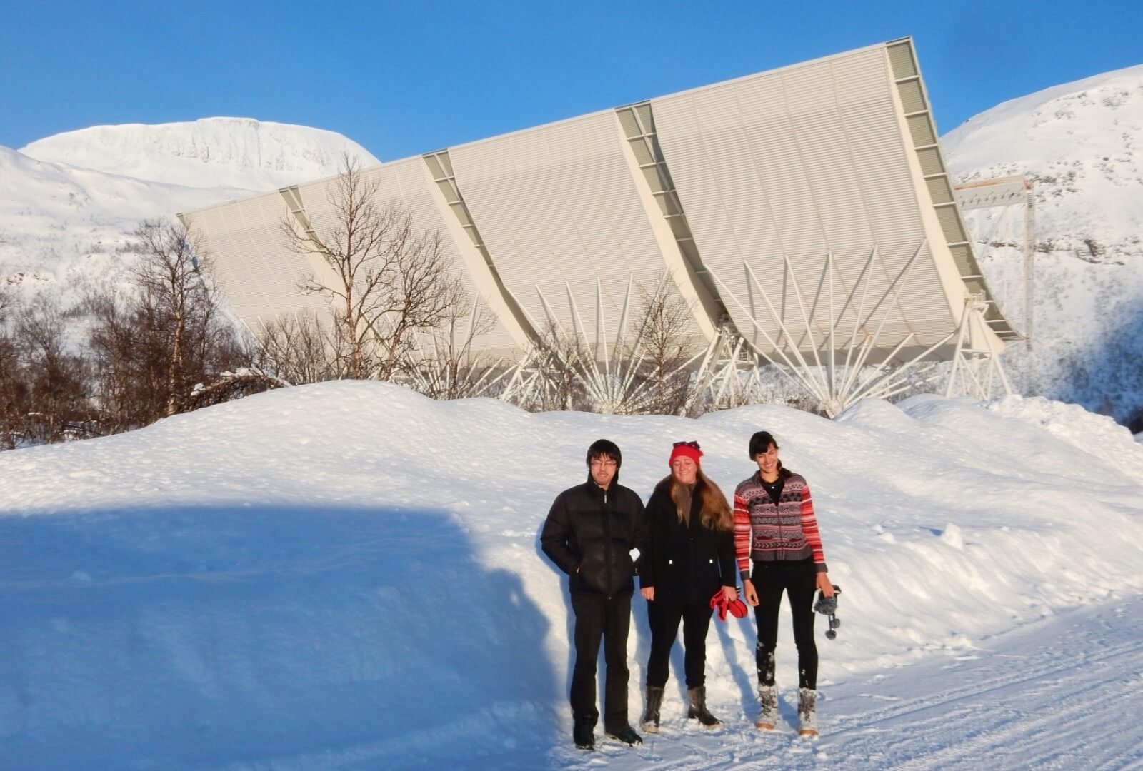 Three students standing by the EISCAT VHF radar array in Norway.