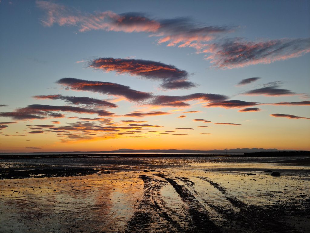 A bright sunset at the beach, with tracks in the sand.