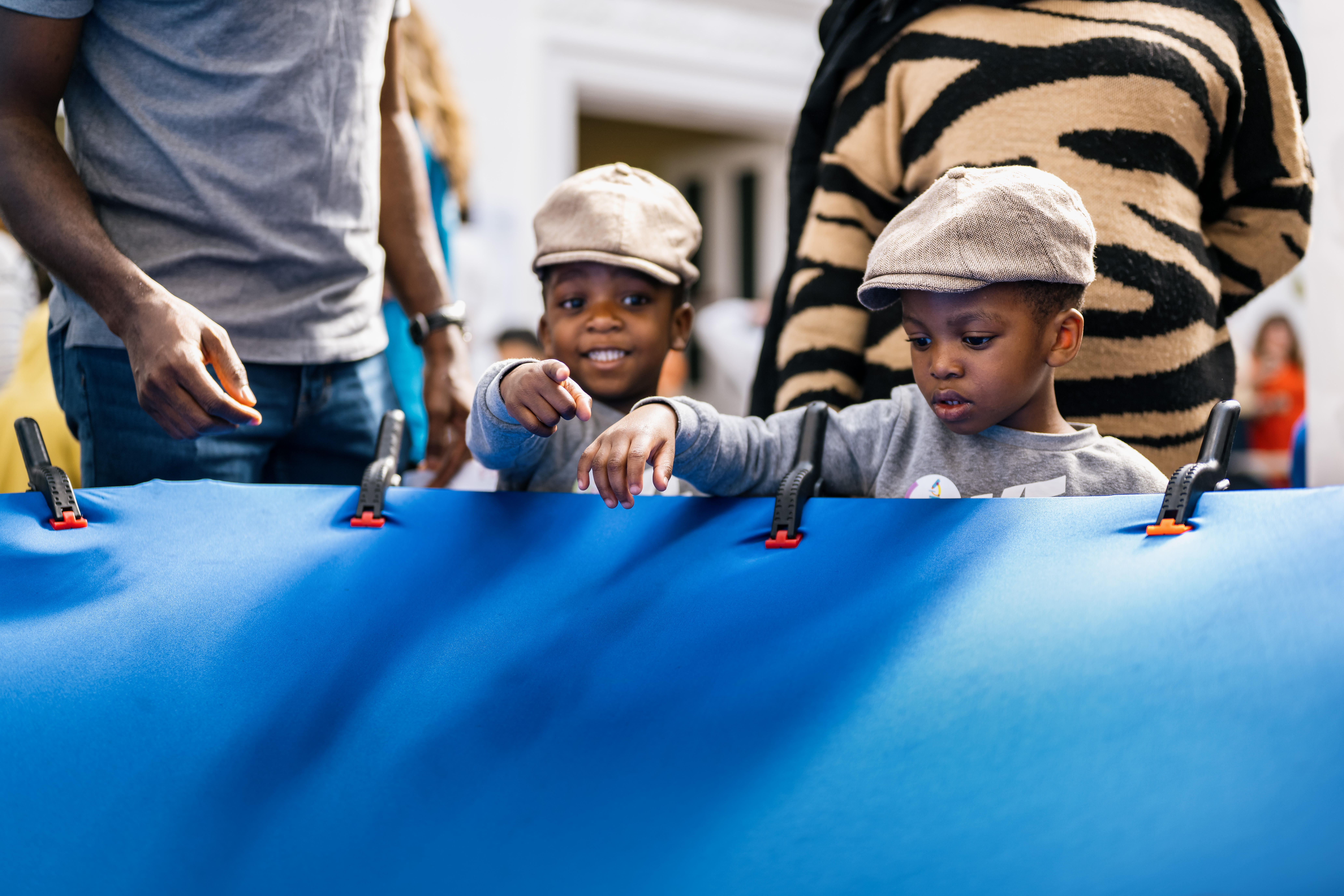two small boys in flat caps hold on to a blue sheet