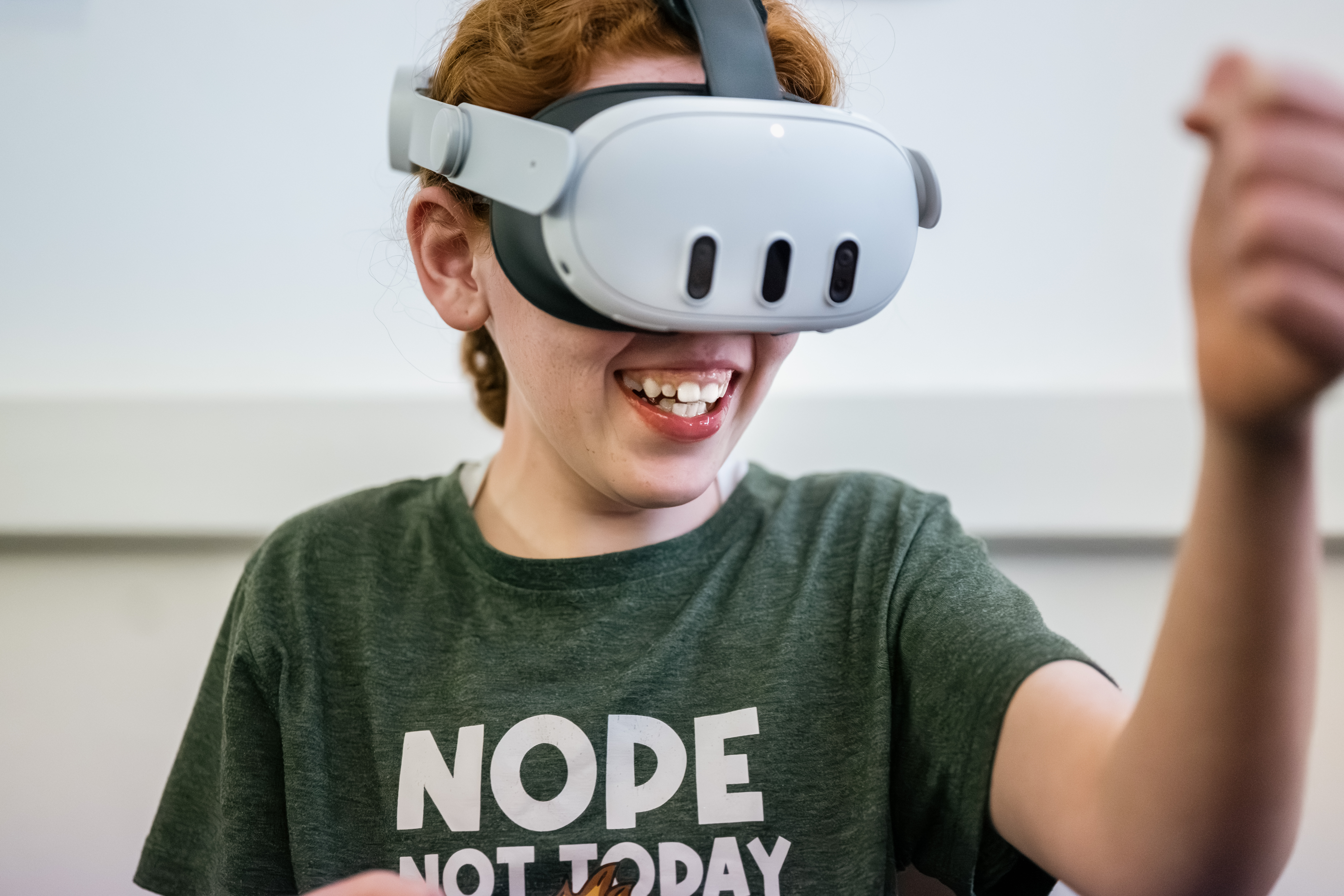 a girl in a green t-shirt reaches out her hand whilst wearing a VR headset