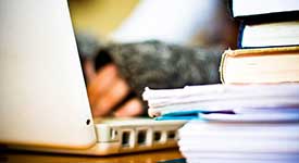 A researcher using a laptop and books to research