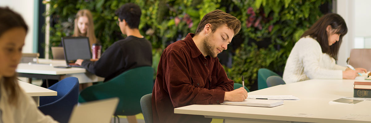 Students study in the library against the backdrop of a wall of plants