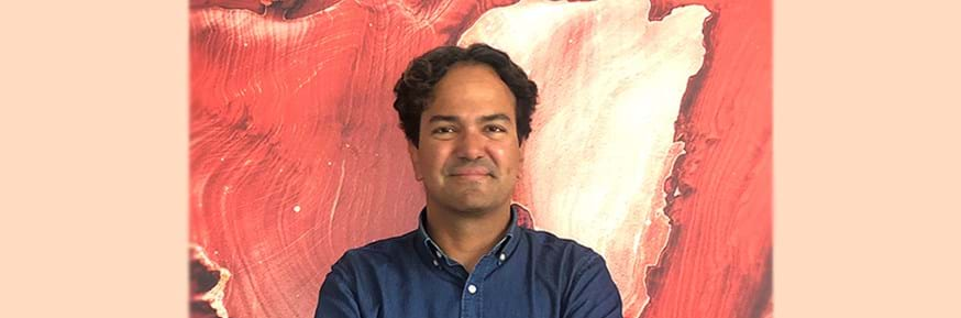 image of Carlos Lopez Galviz stood in front of an orange and peach canvas.