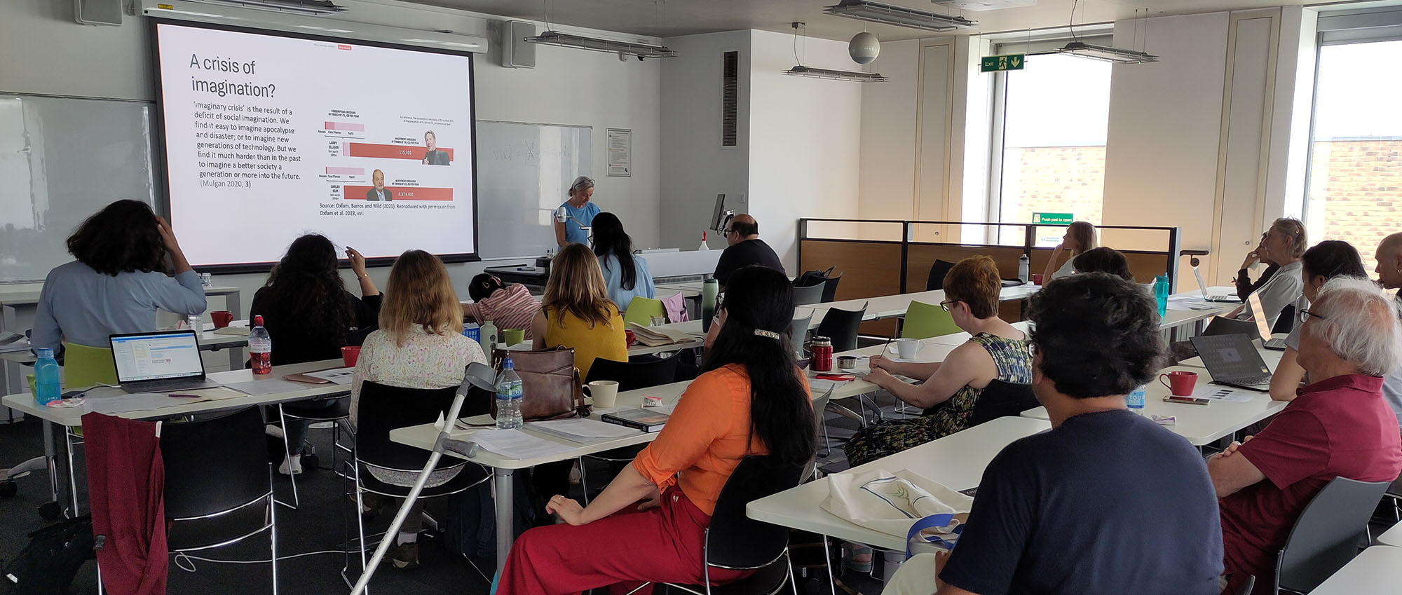 summersymposium2025 Speaker Monika Buscher at the front of a seminar room full of people. The slide reads 'A Crisis of Imagination'.