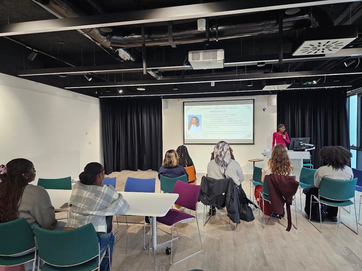 Students and staff sitting in the library listening to a workshop delivered by Victoria Nyoni on hair braiding
