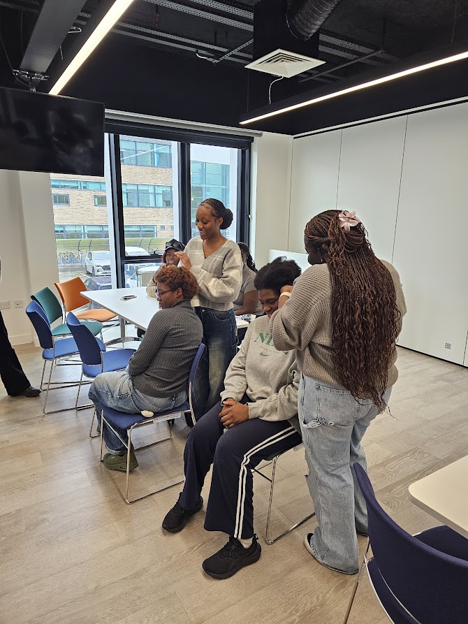 Two female students getting their hair braided by two other students.