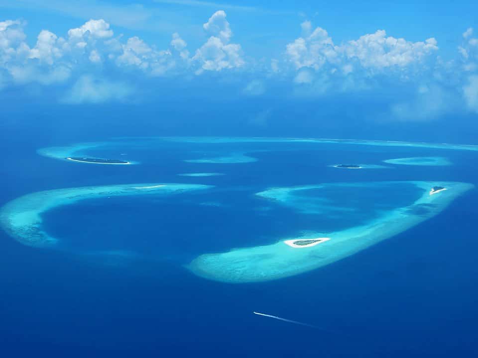 Five small islands made of white sand with sparse greenery in a deep blue ocean.