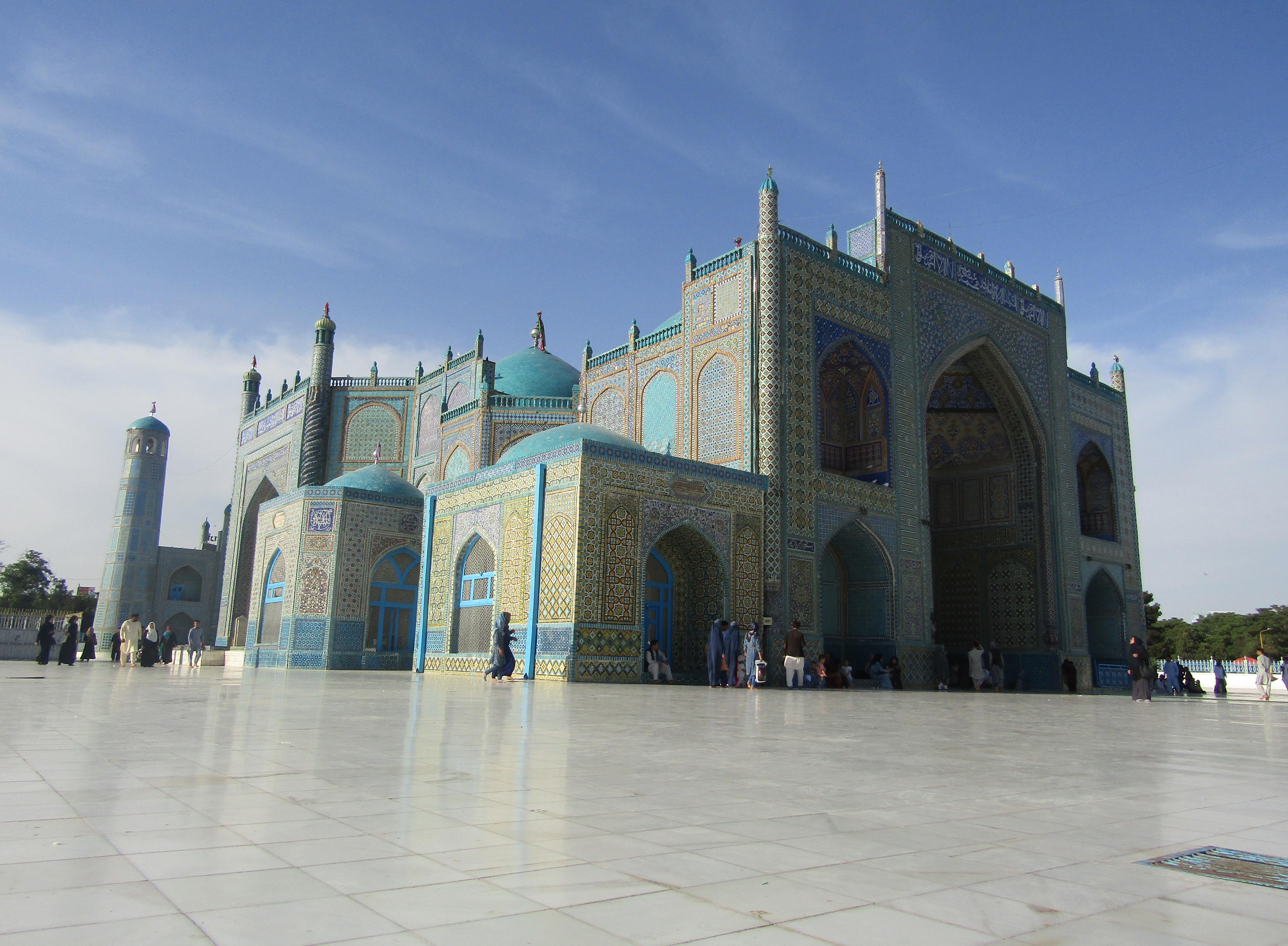 A large mosque covered in blue tiles and with ornate gold tiles in patterns along the outer walls. At the front is a large domed doorway lined with tiles in different patterns.