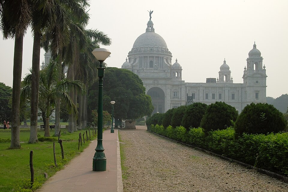 A line of two street lamps next to a large palm trees next to garden path. In the background is a large white monument with a domed roof.