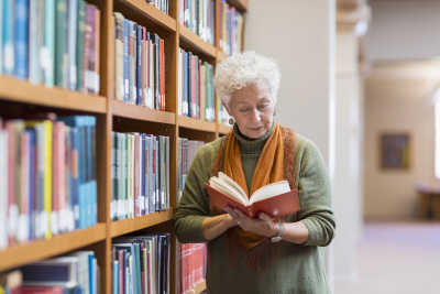 Researcher reading a book stood next to shelves in a library.
