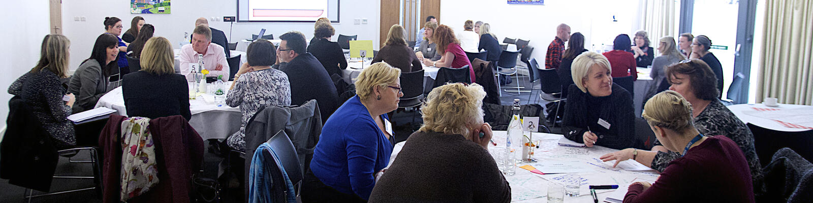 People sit around tables, deep in conversation at a conference.