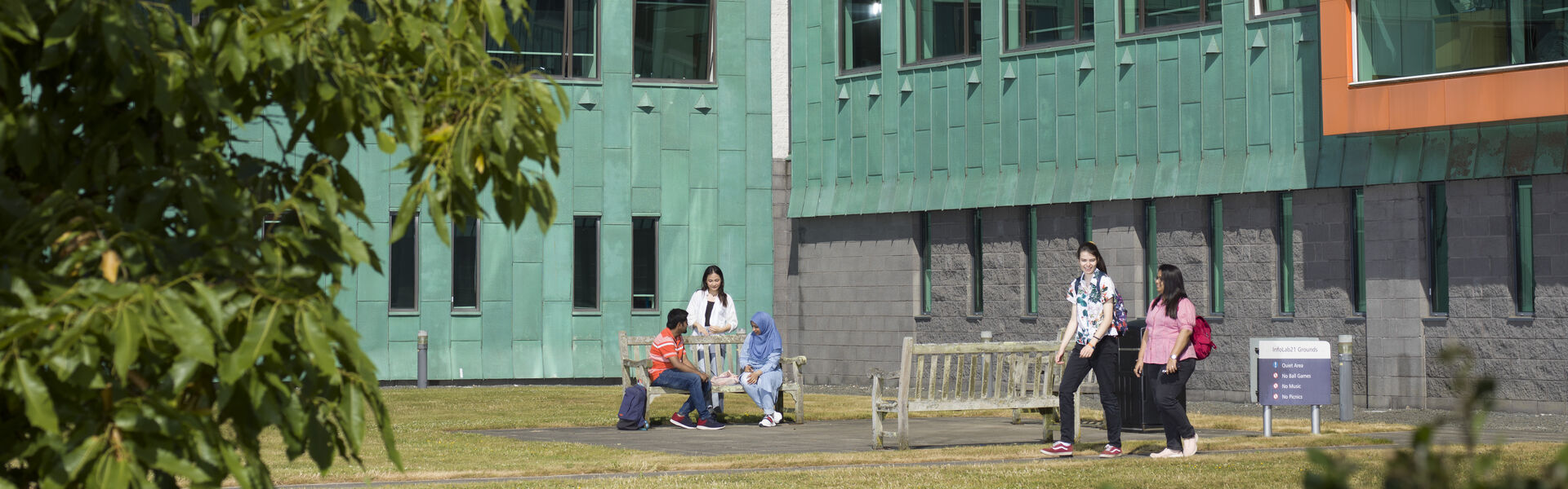 Students socialising outside of Infolab, a green building with large windows