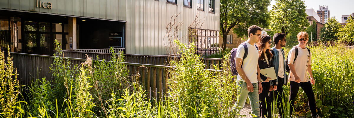 Students walking across LICA building wooden bridge, surrounded by greenery