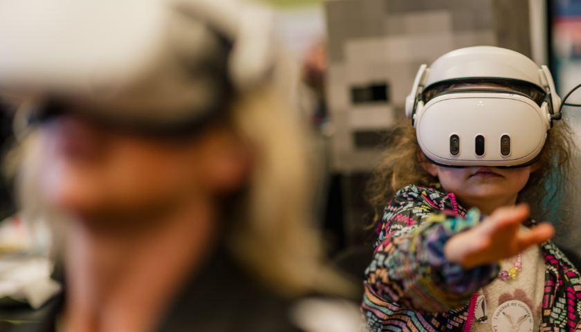 2 people wear VR headets. One person is out of focus.