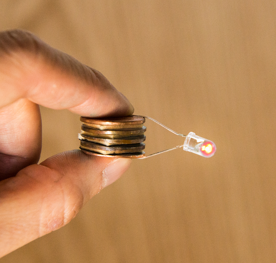 a hand holds a pile of coins attached to a small lightbulb
