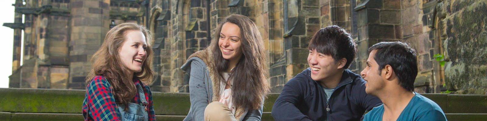 4 students, 2 men and 2 women, sitting down on stone steps in front of the Lancaster Castle.
