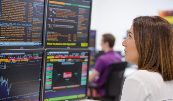 A student at a desk looking at financial information on four computer screens
