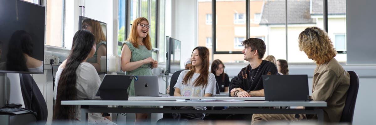 A tutor leads a discussion with students around a table in a bright teaching space.