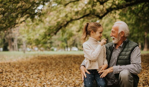 Grandfather spending time with his granddaughter in park on autumn day
