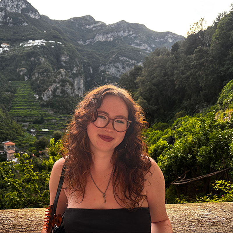 Student, Izzi posing in front of vast green trees