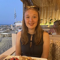 Katie sat at a table with a plate of food in front of her and a beach scene in the rear