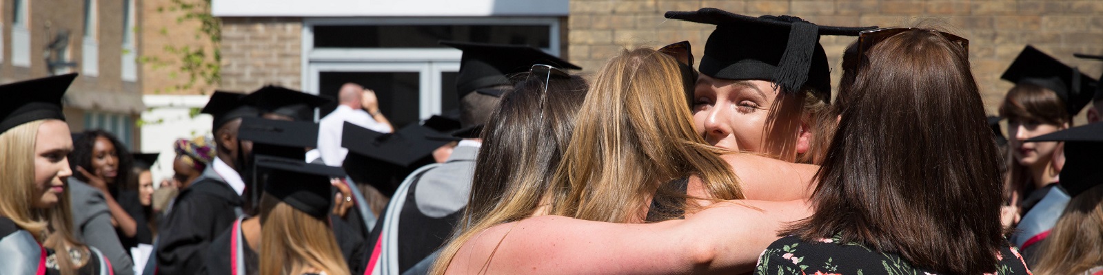 Family hugging a student just graduated wearing graduation robes