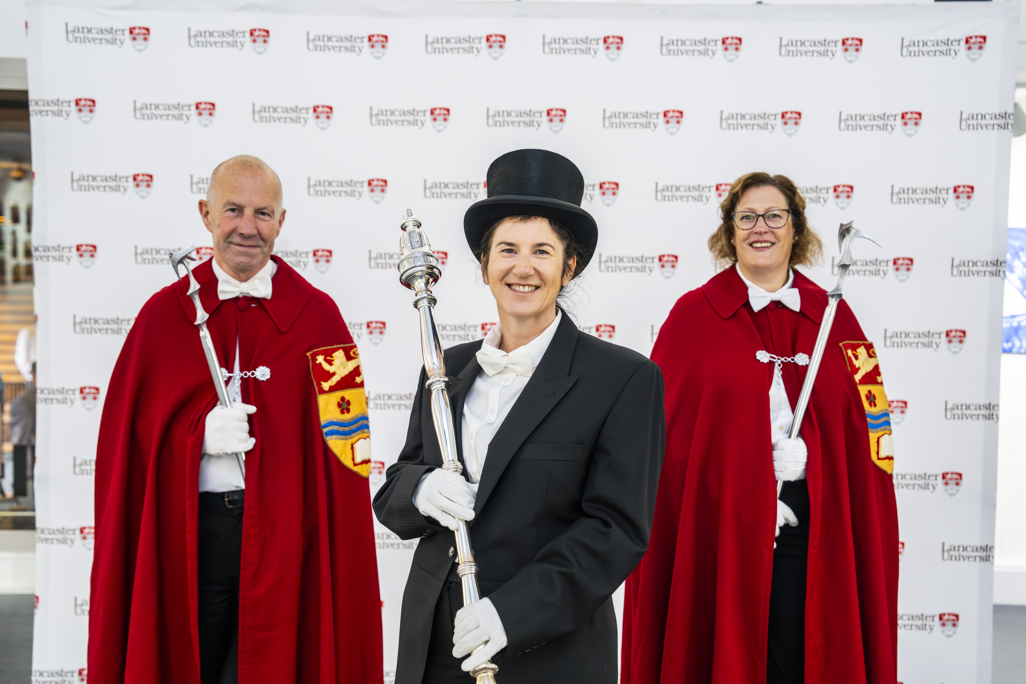Photo shows three staff members dressed in graduation regalia and holding ceremonial pieces
