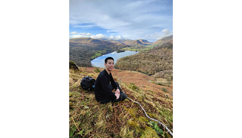 Daniel Chin on top of a hill in the lake district overlooking a lake