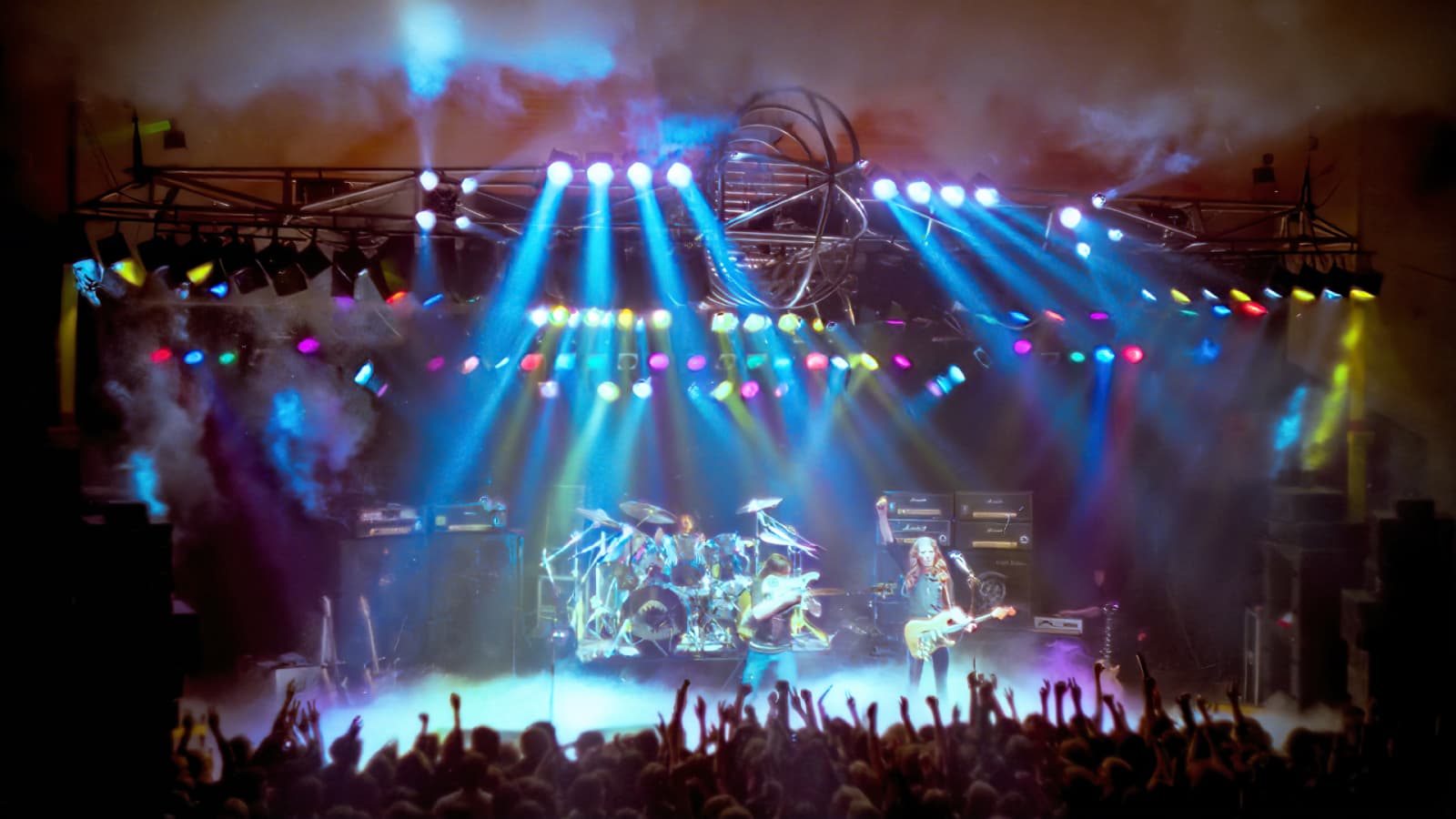 Motörhead play on stage underneath a large lighting rig shaped like an aeroplane.