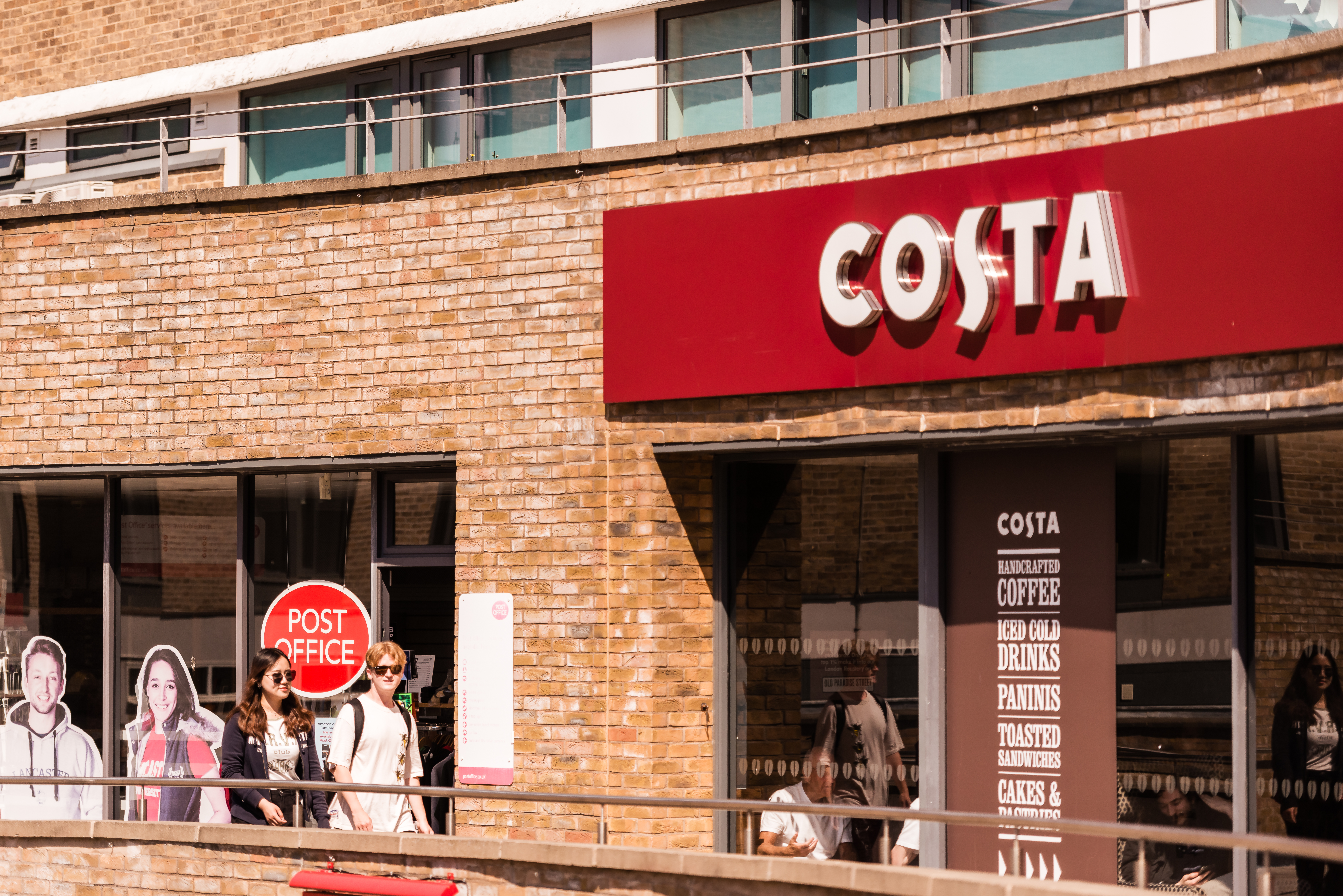 Two students walking past Costa Coffee located within Edward Roberts Court, Lancaster University
