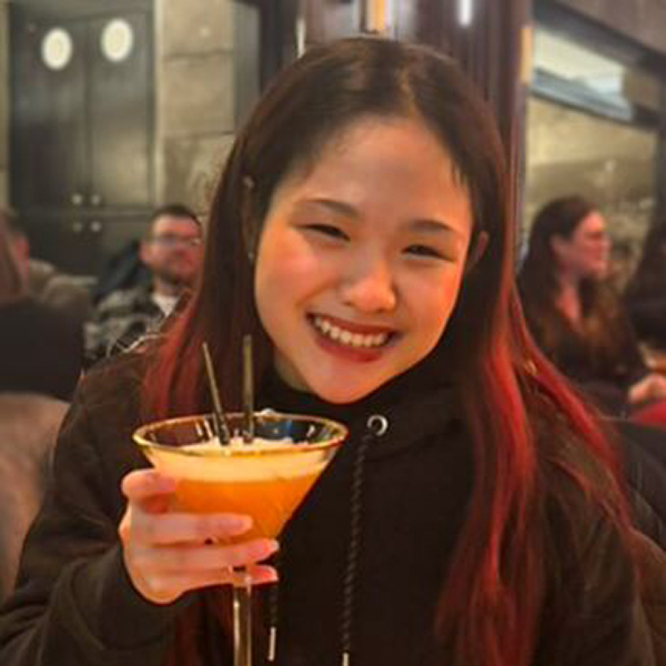 Image of student Cha-ame smiling at the camera, holding a drink up