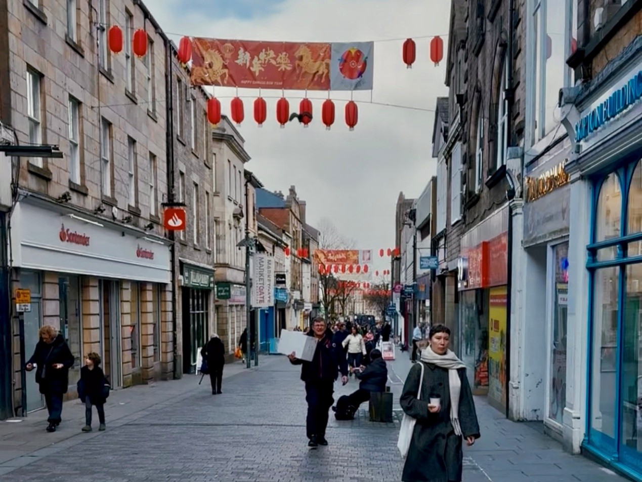 A street in Lancaster town centre full of Chinese New Year decorations and with people walking around. 