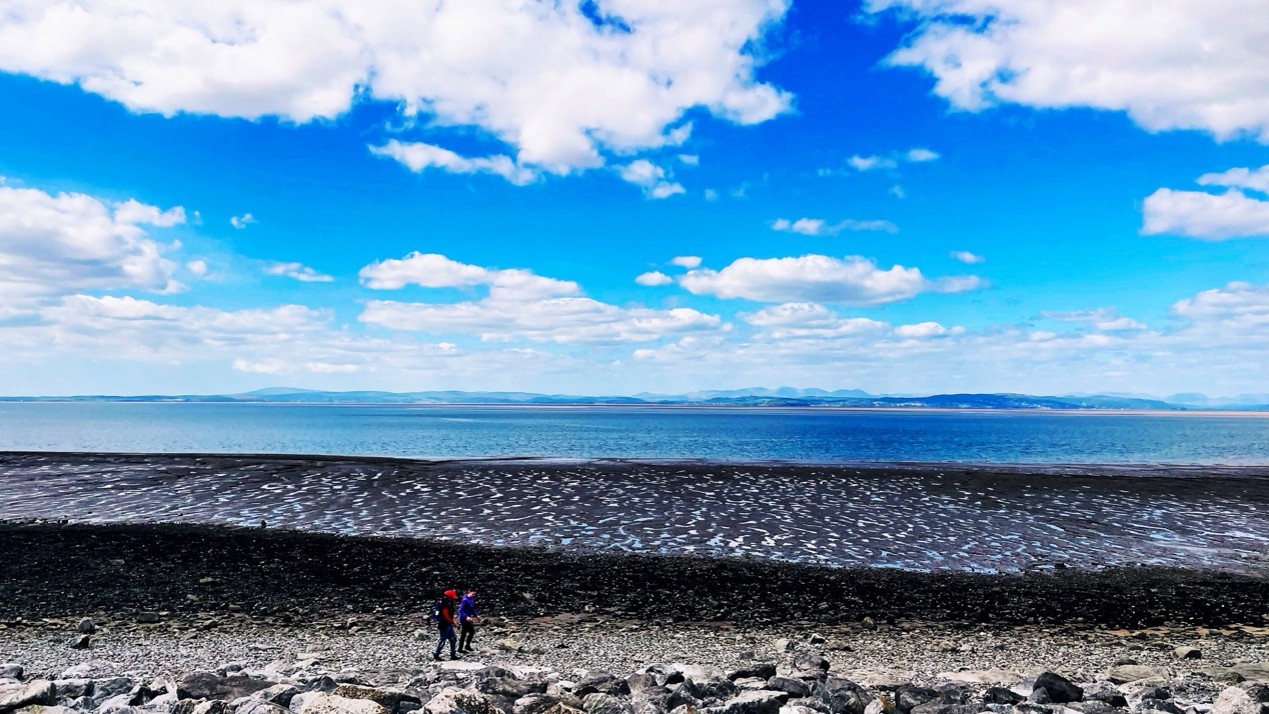 The beach in Morecambe with two people walking on it on a sunny day.