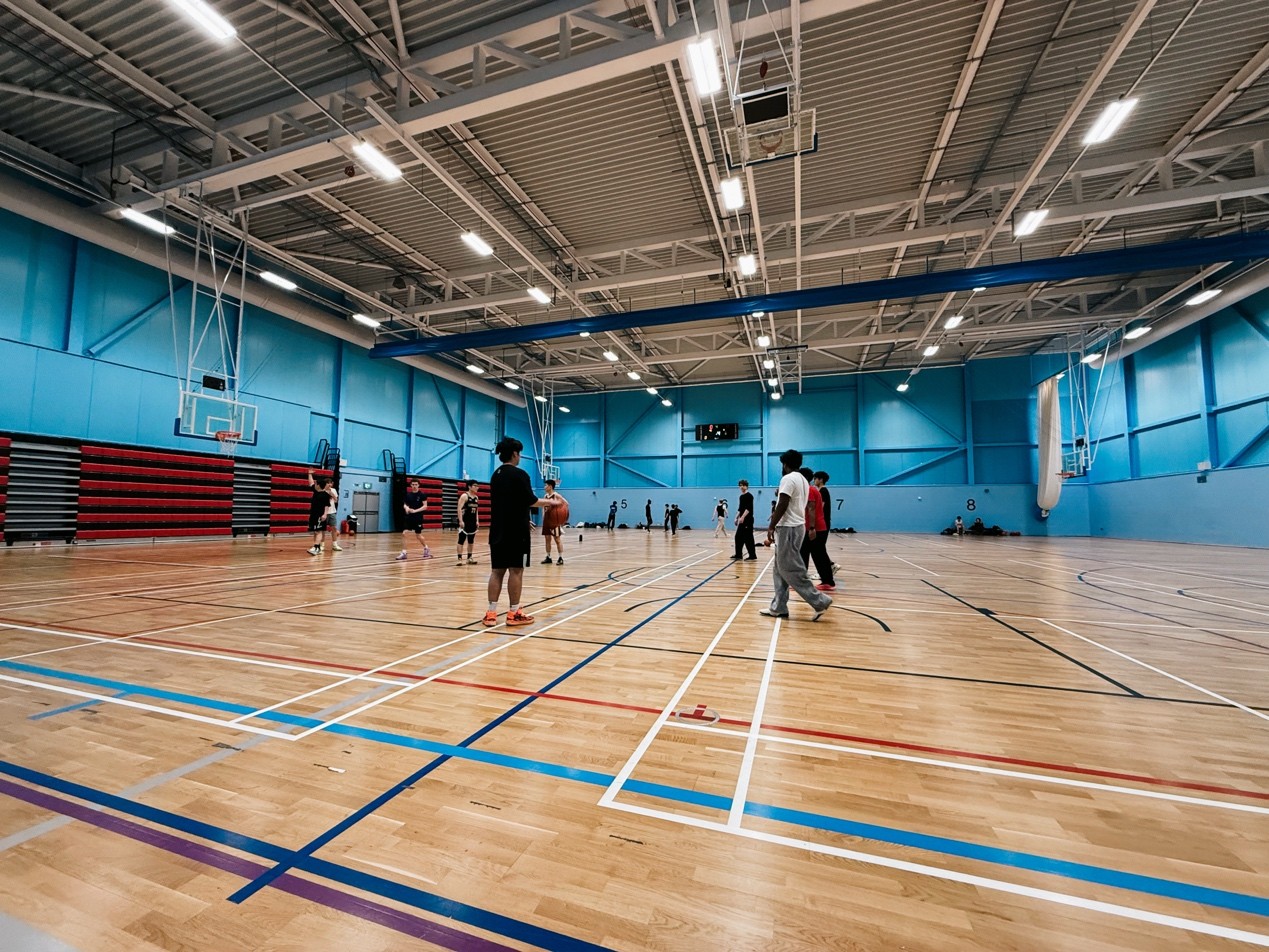 A group of people playing basketball in the basketball court at sports centre.