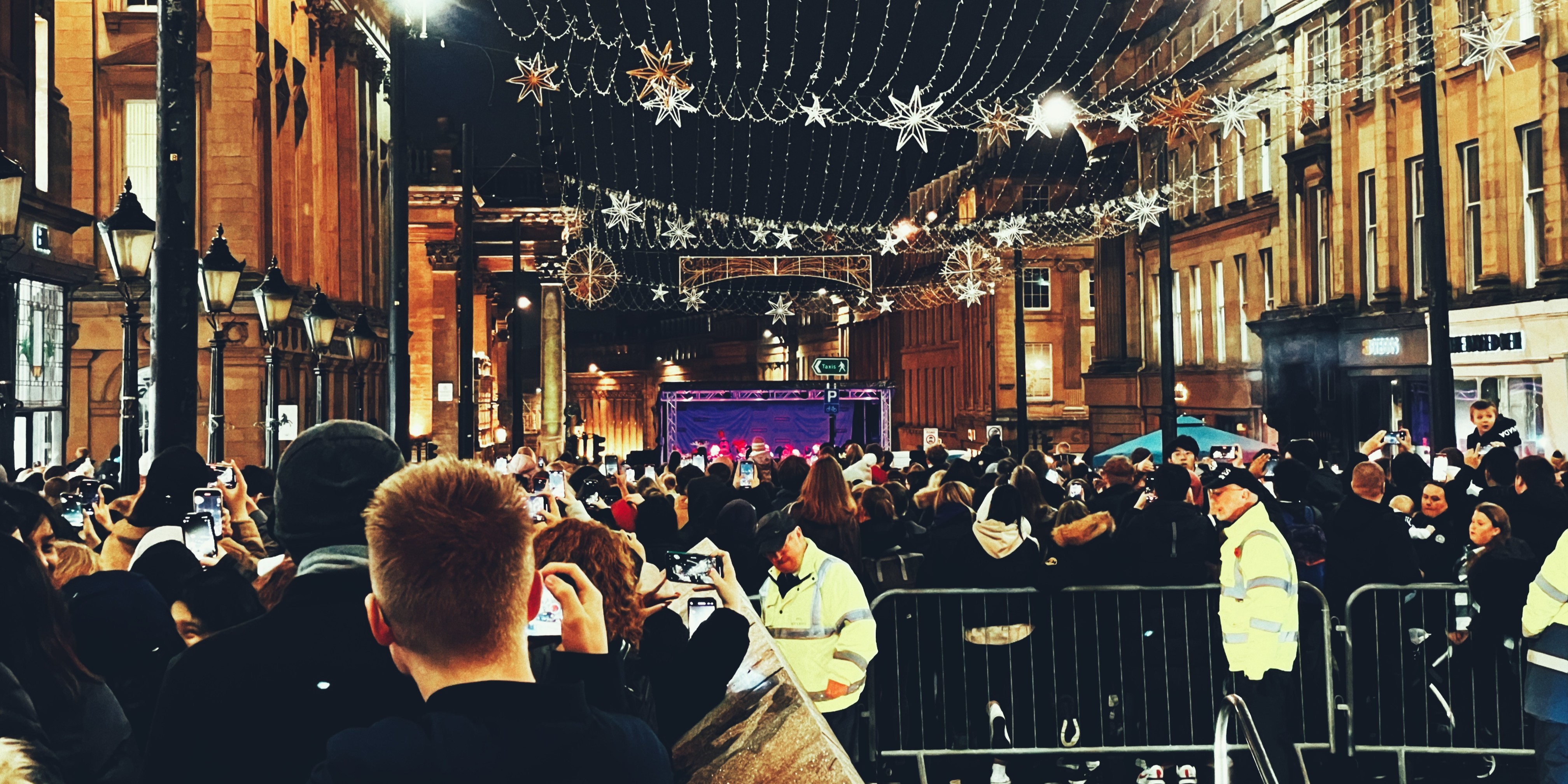 A crowd of people in town along the street watching a live performance. 