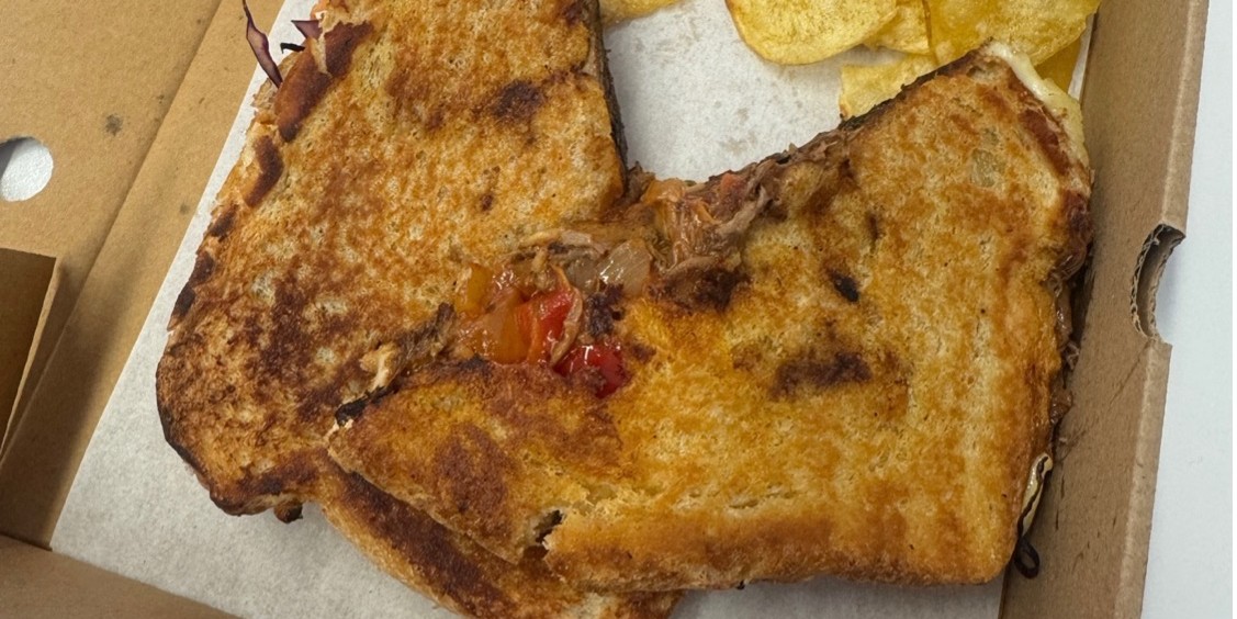 A beef brisket and cheese toastie with crisps on the side.