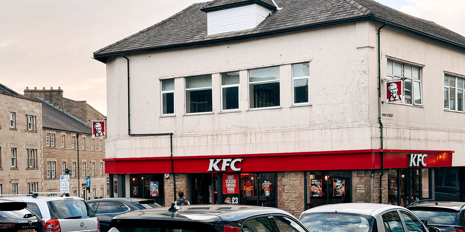 A KFC in Lancaster town centre with cars parking along the road.