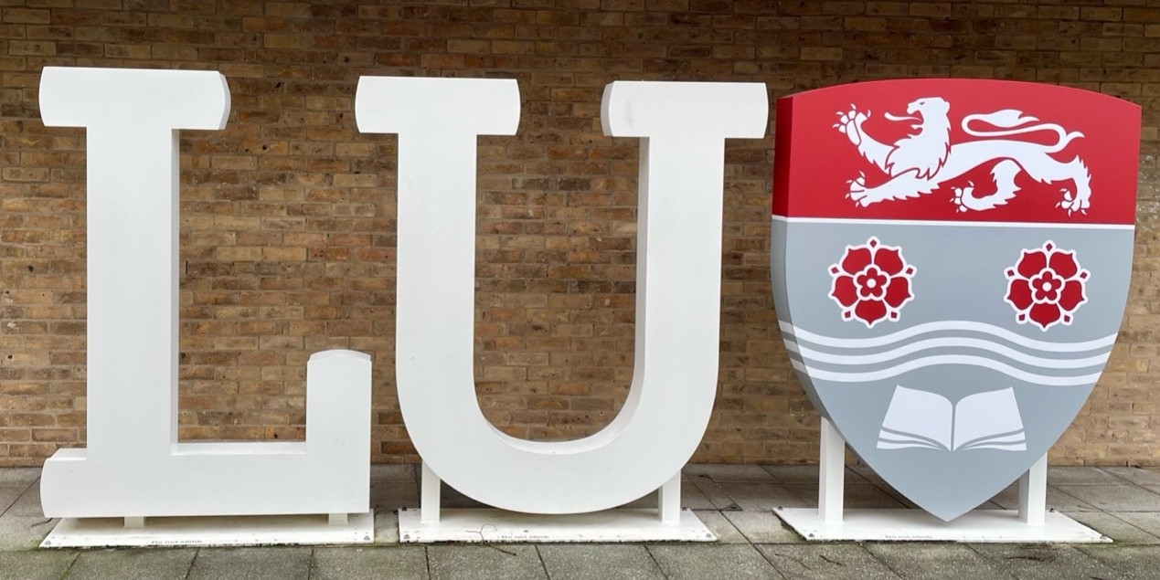 A sign of the letter LU and a red and grey shield of Lancaster university logo.
