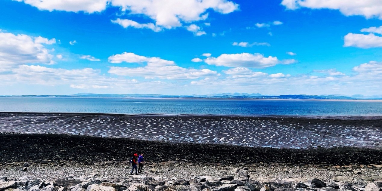 The beach in Morecambe with two people walking on it on a sunny day.