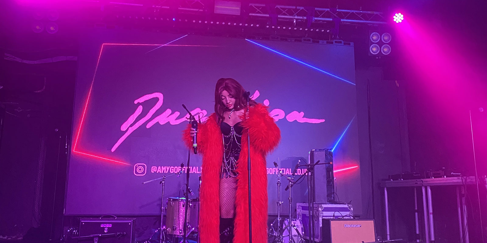 A person stands at the microphone, ready to sing on a stage bathed in purple and pink light.