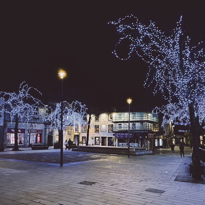 Lancaster town centre at night with shops and people around. 