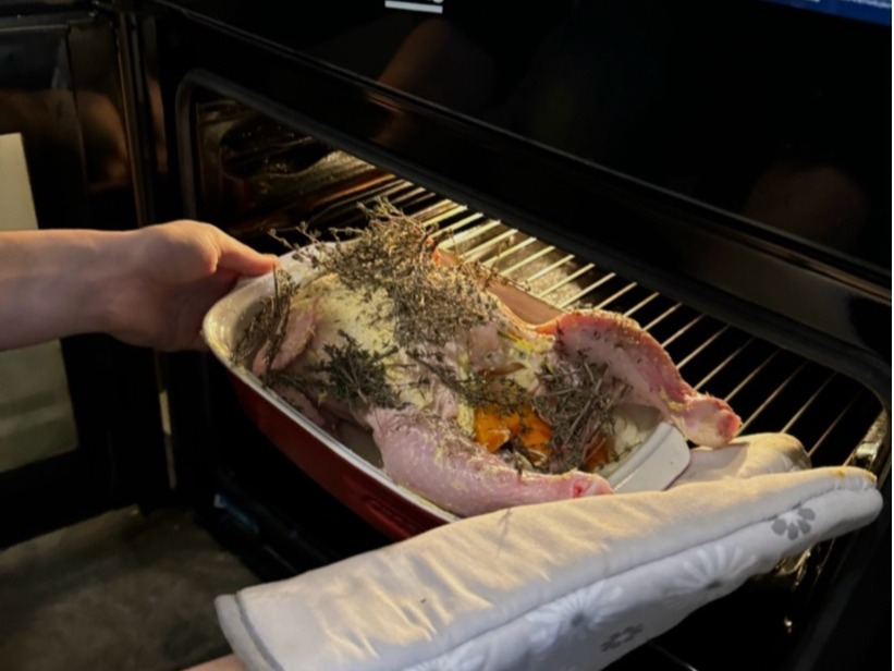 A person putting a roast chicken in the oven.