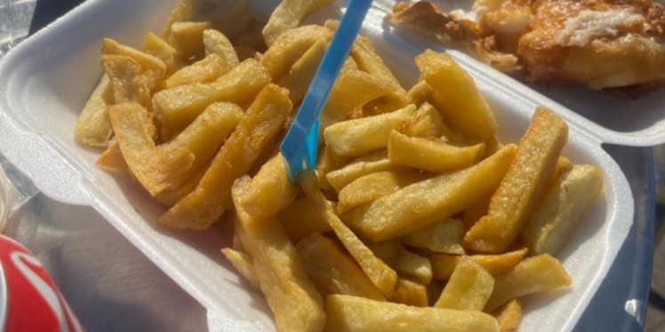 Two people sharing a fish and chips on a sunny day with cokes.