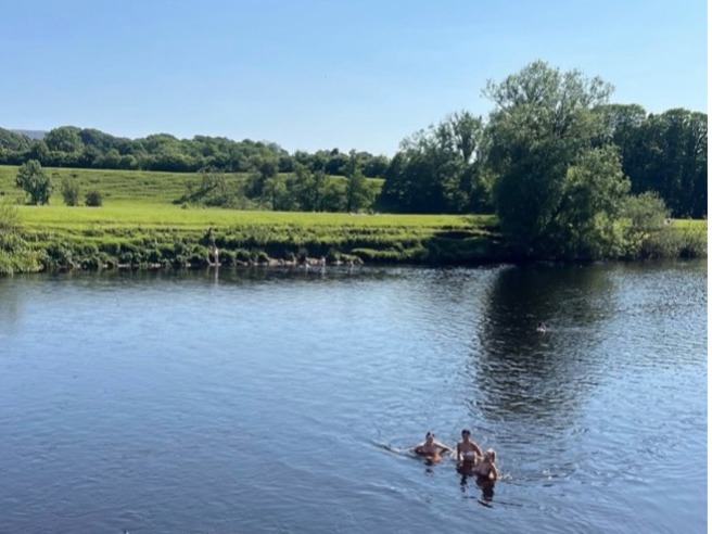 Three people in swimsuits enjoying the River Lune at Crook o' Lune on a sunny day.