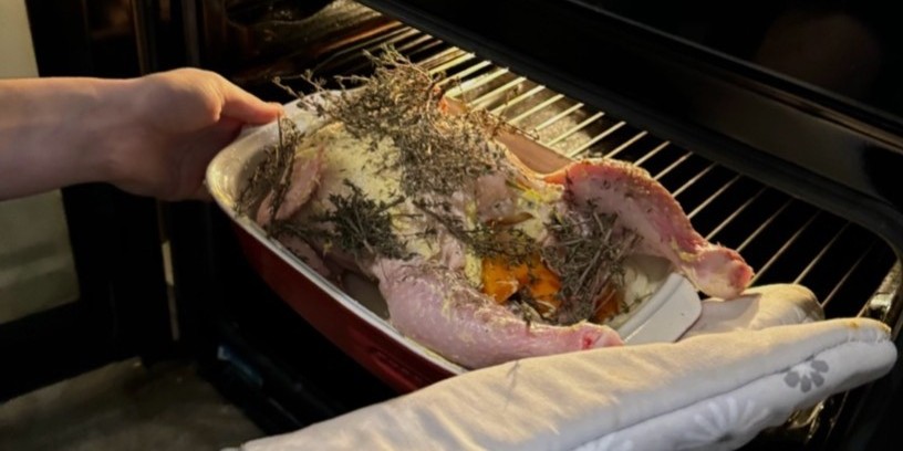 A person putting a roast chicken in the oven.