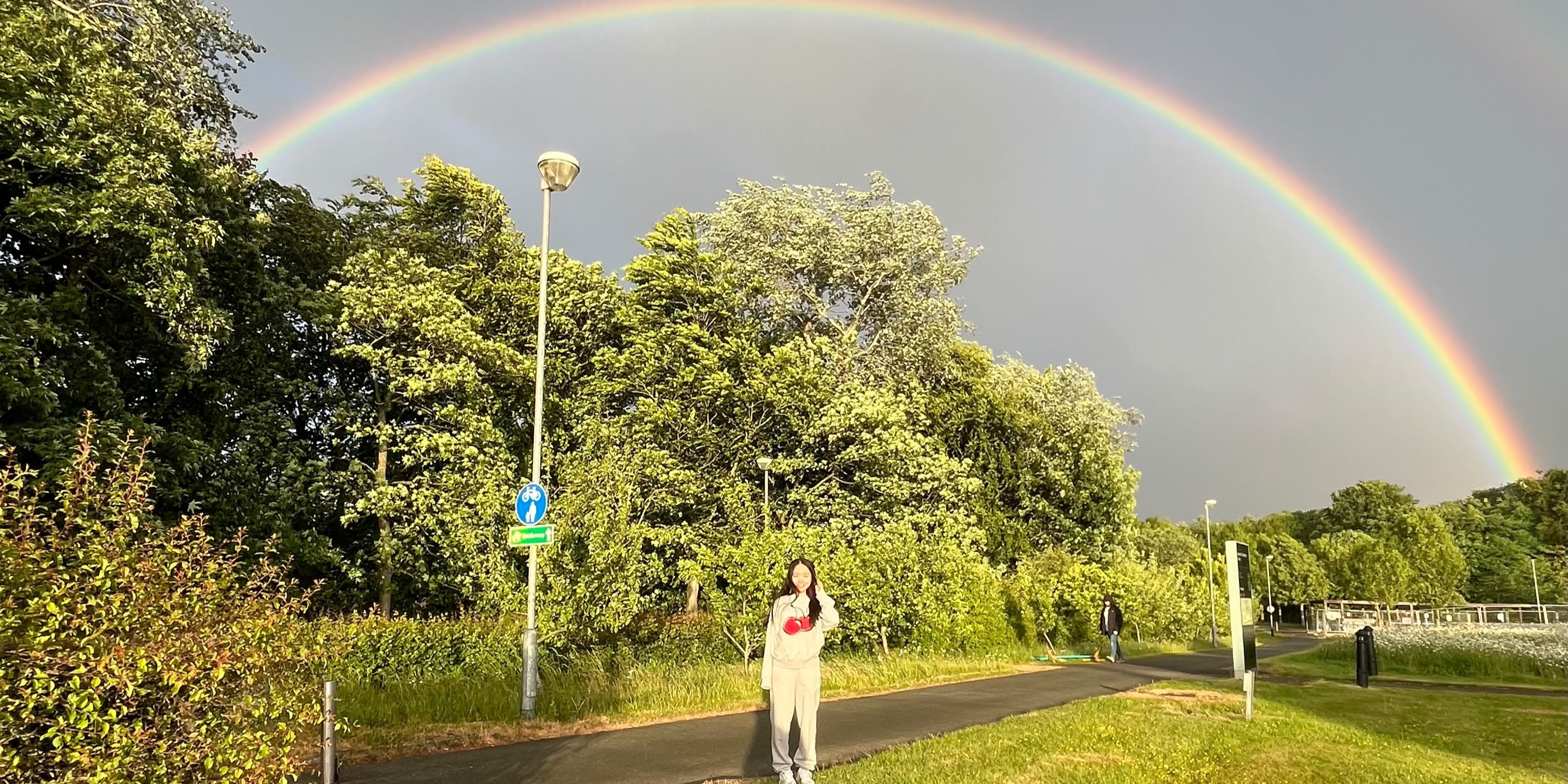 A person on the pavement with a rainbow above her head.