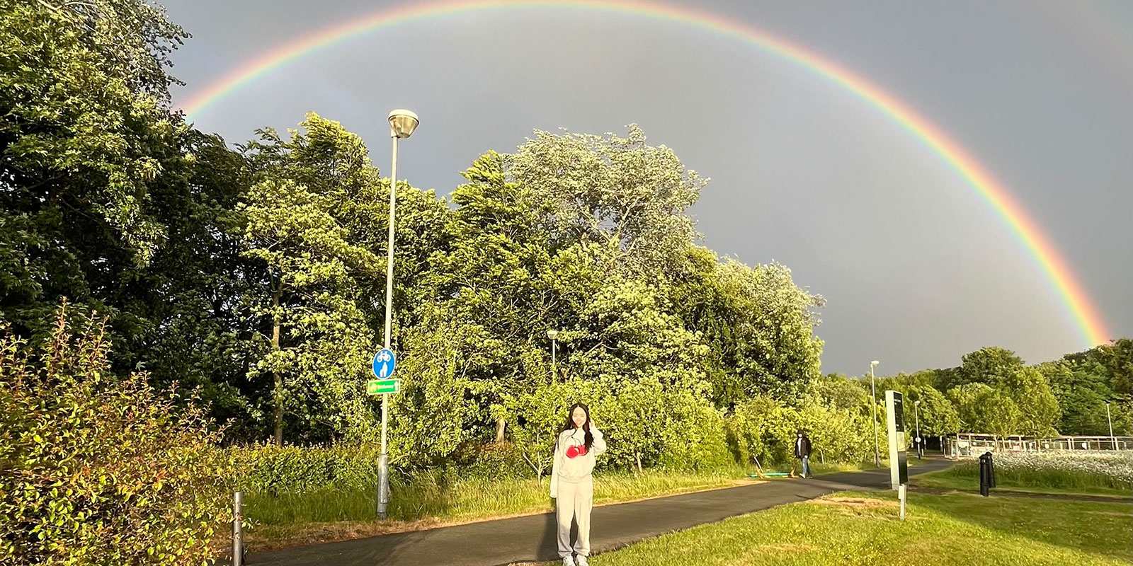 A person on the pavement with a rainbow above her head.