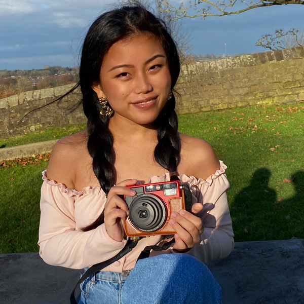 A female student sitting on the grass holding a camera