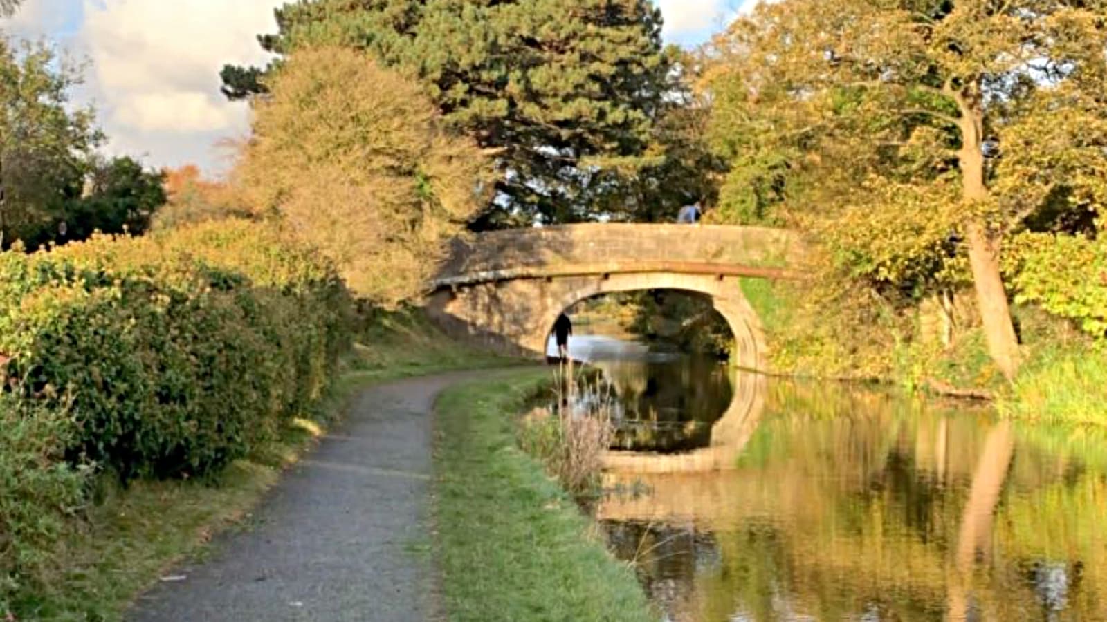 A view along the canal towpath with a bridge and trees