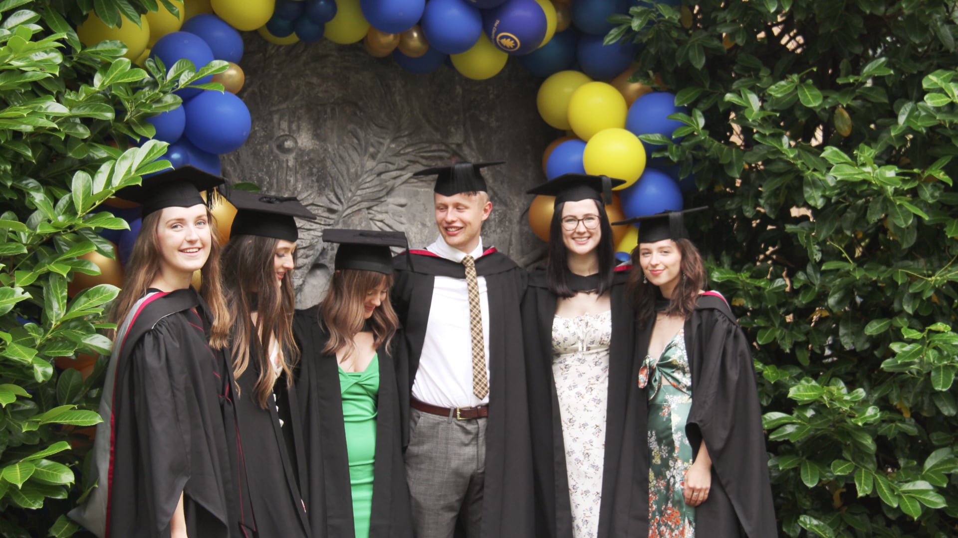 Catherine and her friends stand underneath an archway of balloons